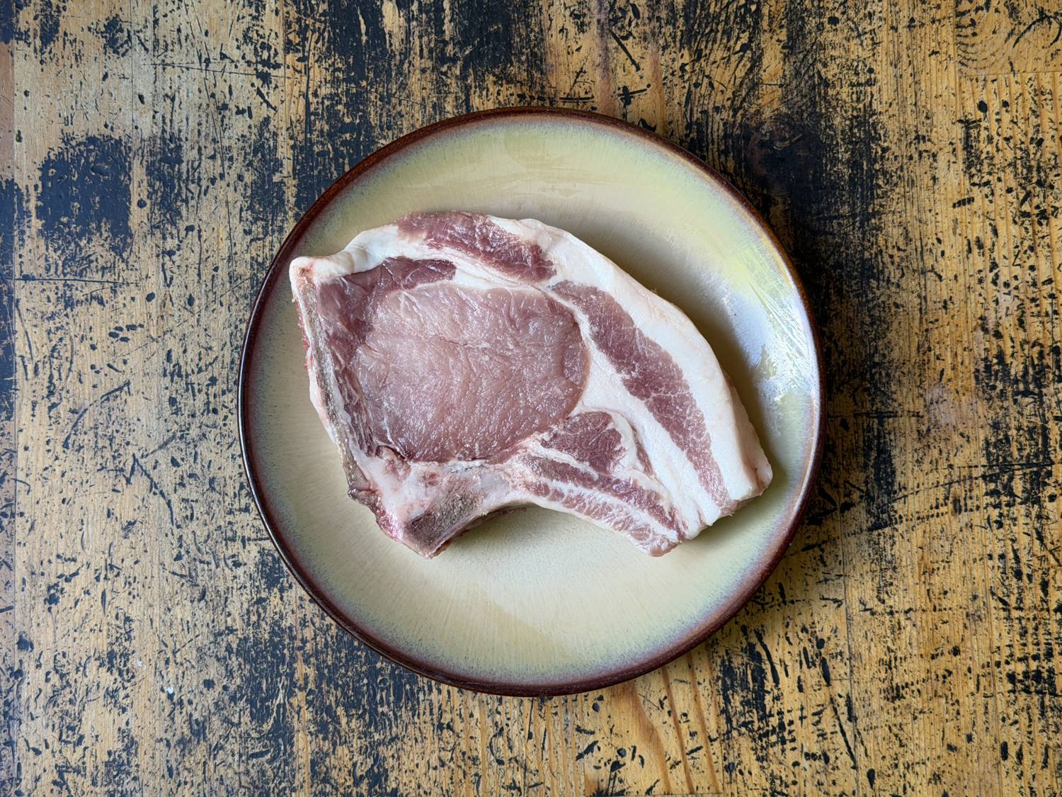 A raw bone-in pork chop from Woodcock Livestock showing rich marbling